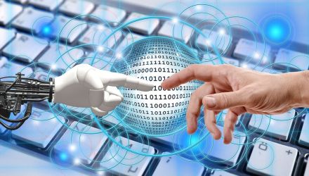 Z lewej robotyczna ręka sięga do ludzkiej ręki z prawej, na tle klawiatury komputerowej.