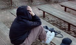 A teenage girl in a black hoodie with a hood on her head is sitt