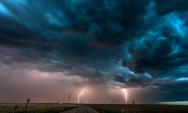 A nighttime, tornadic mezocyclone lightning storm shoots bolt of electricity to the ground and lights up the field and dirt road in Tornado Alley.