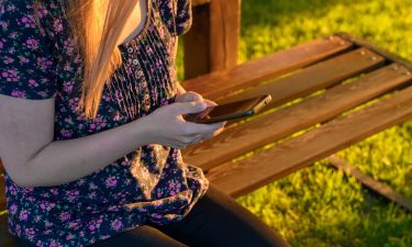 Kobieta siedzącą na ławce w parku korzystająca z telefonu komórkowego