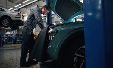 Male in protective clothes standing in tire fitting near car with open hood and checking