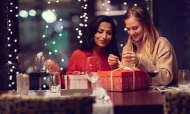 Two adolescent women going through the menue  in a fancy restaurant, while drinking a glass of red wine and laughing and talking, maybe gossiping