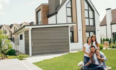 Family sitting on lawn in backyard, big modern house on background
